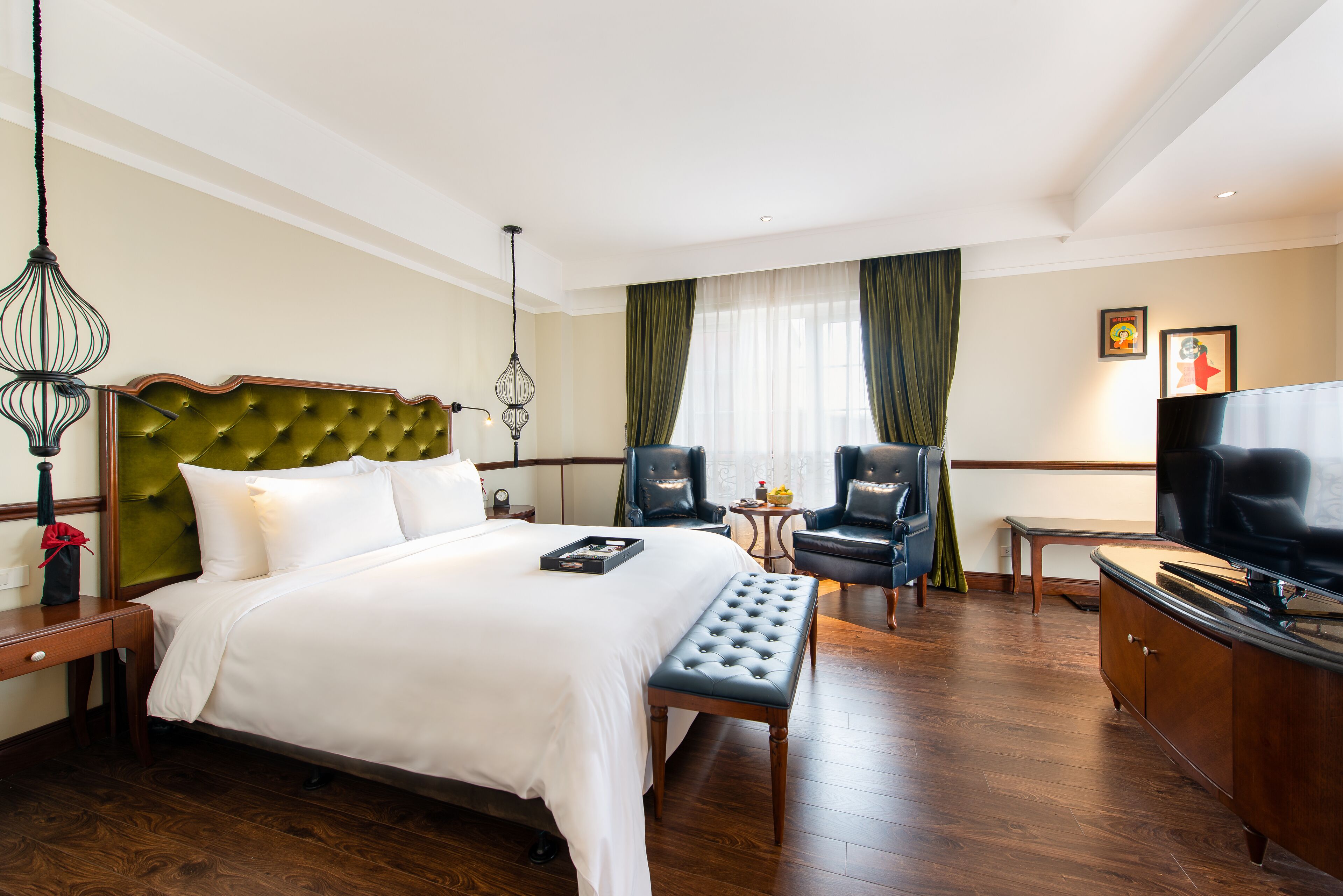 Habitación de hotel con una cama grande, un banco, dos sillones, una mesita, un televisor y un armario.