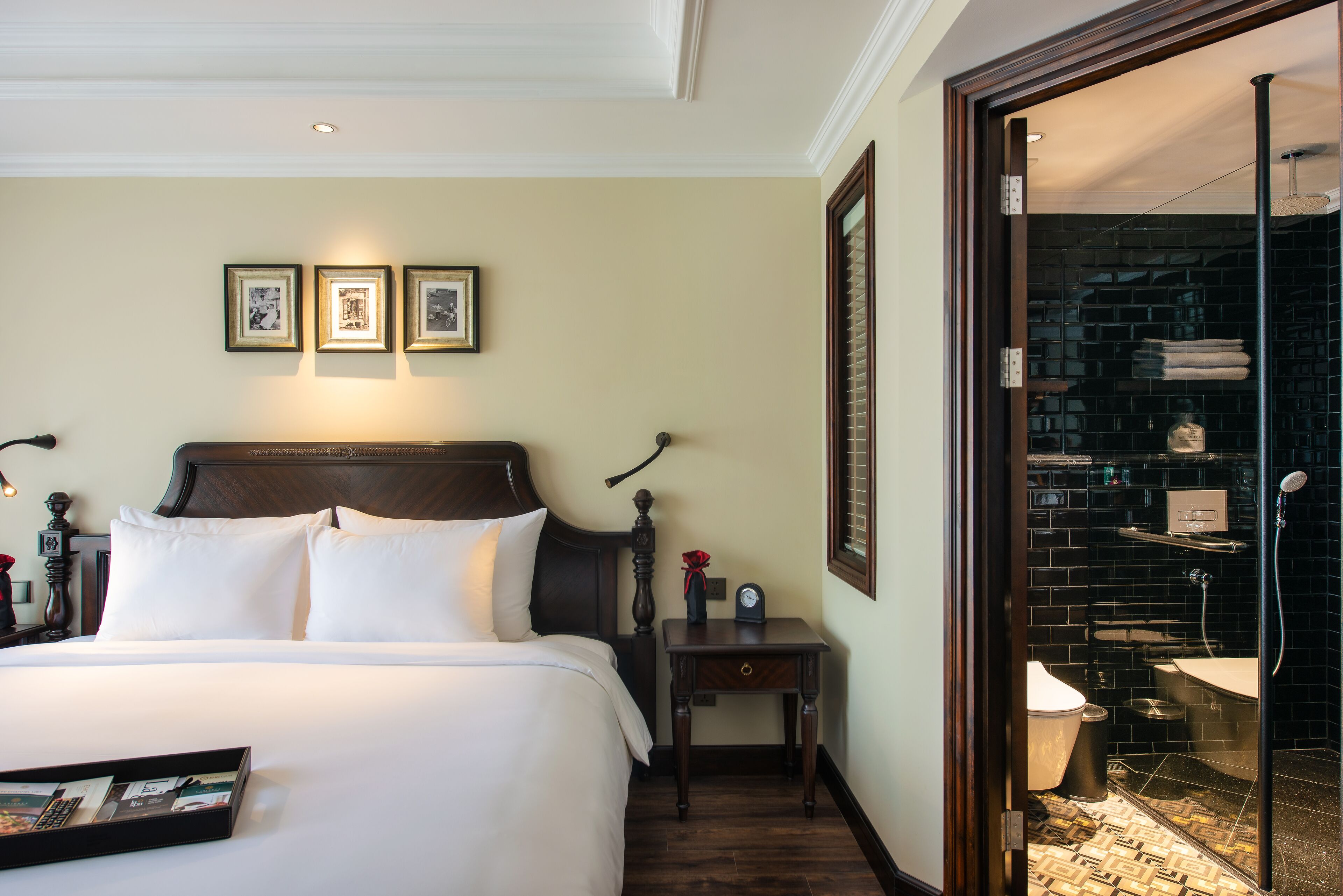 A hotel room with a large bed, a nightstand, a framed picture above the bed, and a bathroom visible through an open door.