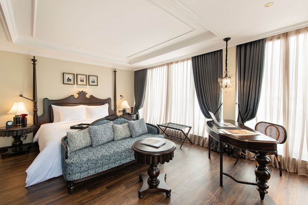 A hotel room with a large bed, a sofa, a round coffee table, a dining table, and curtains.