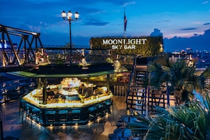 Een bar genaamd 'MOONLIGHT SKY BAR' met een toog, zitplaatsen en uitzicht op de skyline.