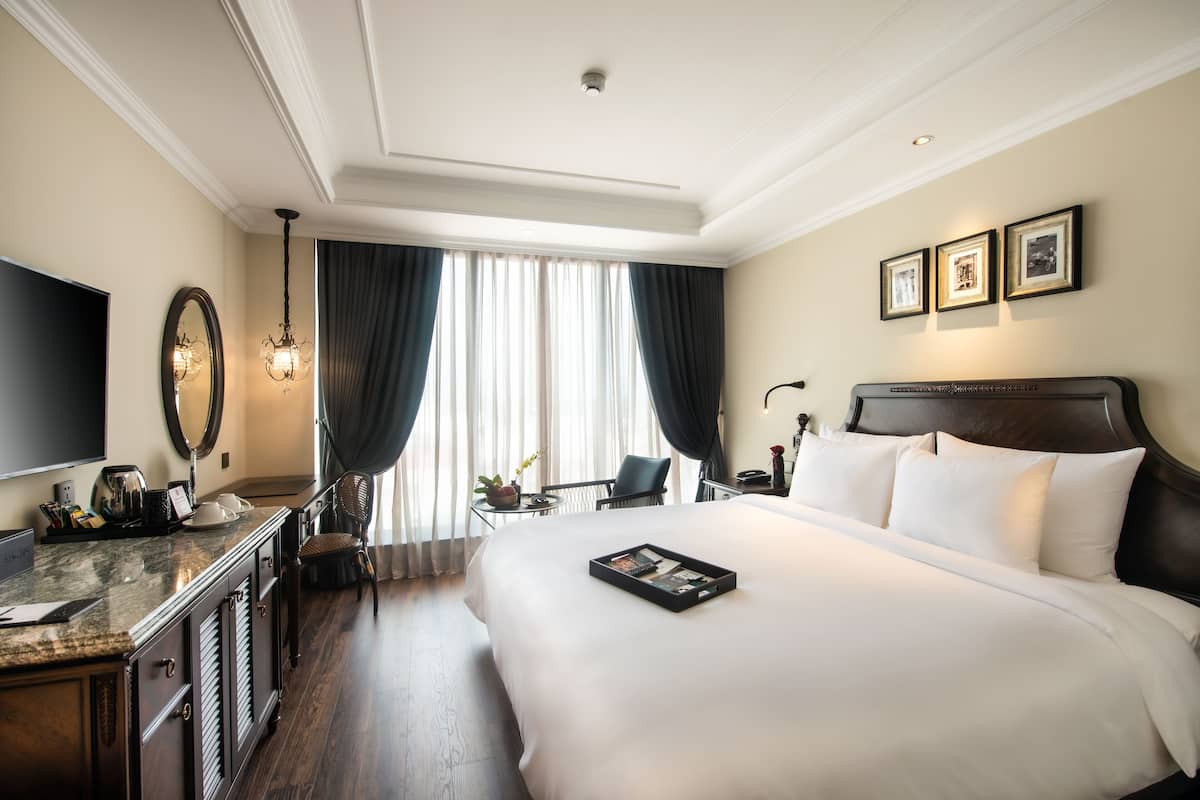 A hotel room with a large bed, a desk with a flat-screen TV, a mirror, and a window with curtains.