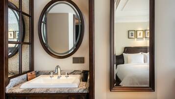 A bathroom with a marble sink, a large mirror, and a framed bed reflection.