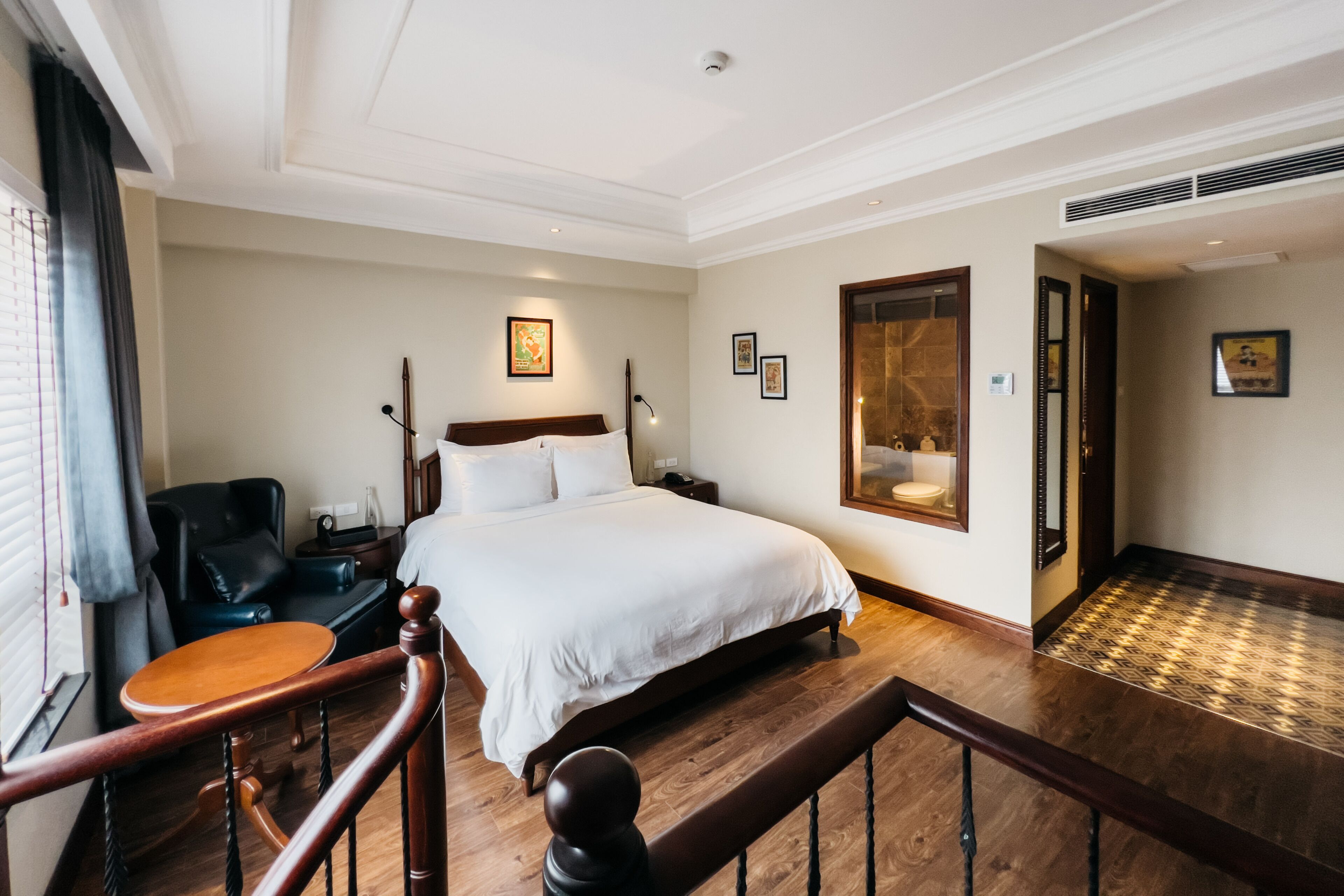 A hotel room with a large bed, a wooden desk, a chair, a nightstand, and a mirror.