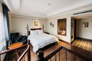 Una habitación de hotel con una cama grande, un escritorio de madera, una silla, una mesita de noche y un espejo.