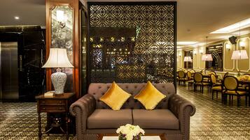 Un vestíbulo de hotel con suelo estampado, un sofá marrón con cojines amarillos, una mesa con un jarrón de flores y una pared decorativa con patrones geométricos.