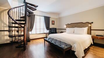 Een slaapkamer met een groot bed, een houten bankje, een bureau en een spiltrap.