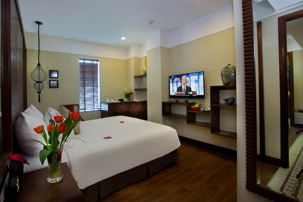 A hotel room with a large bed, a TV, a vase with flowers, and a wooden dresser.