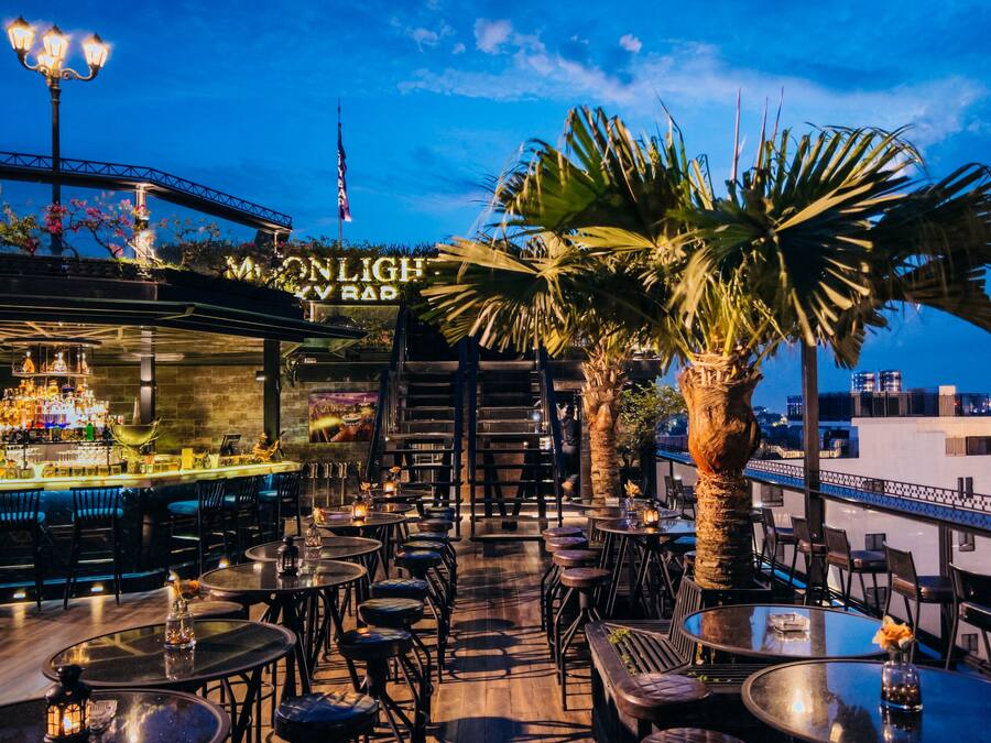 A rooftop bar with a view of the city skyline, featuring outdoor seating and a bar area with a variety of bottles.