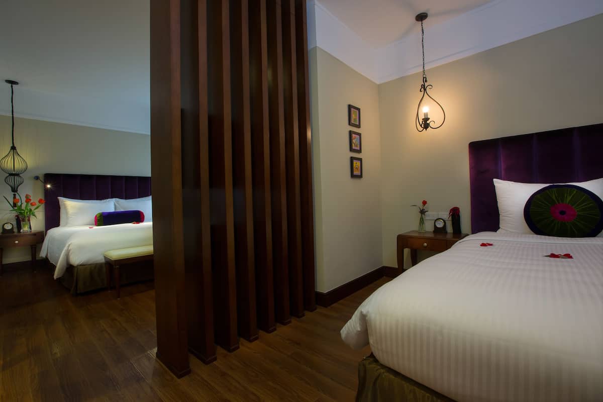 A hotel room with two beds, wooden floors, a dark headboard, and a wall-mounted light fixture.