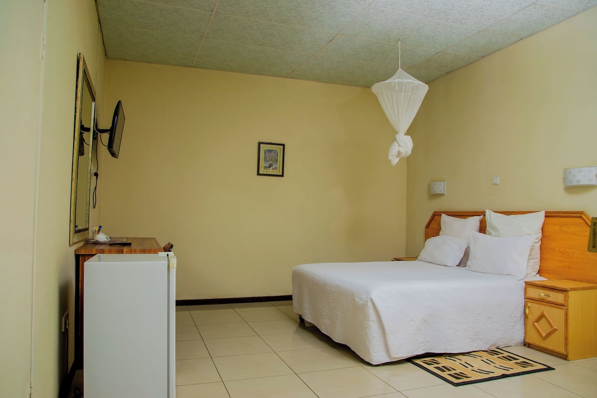 A bedroom with a bed, a nightstand, a bedside table, a wall-mounted mirror, and a ceiling fan.