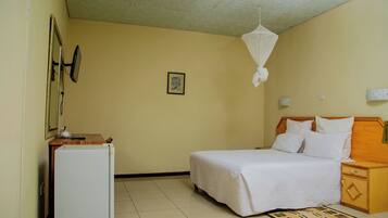 A bedroom with a bed, a nightstand, a bedside table, a wall-mounted mirror, and a ceiling fan.