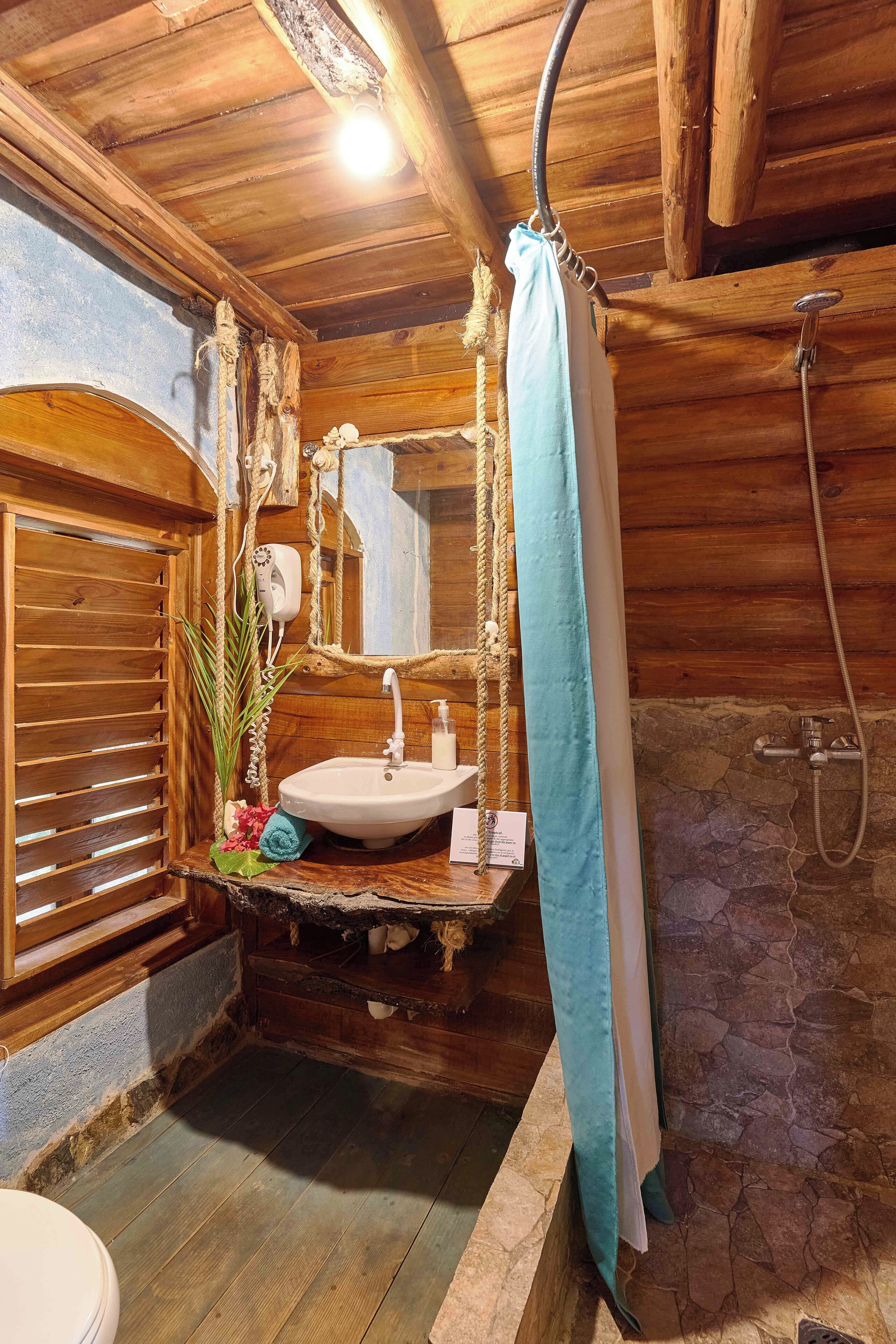 A rustic bathroom with a wooden vanity, a sink, a mirror, a shower with a curtain, and a stone wall.