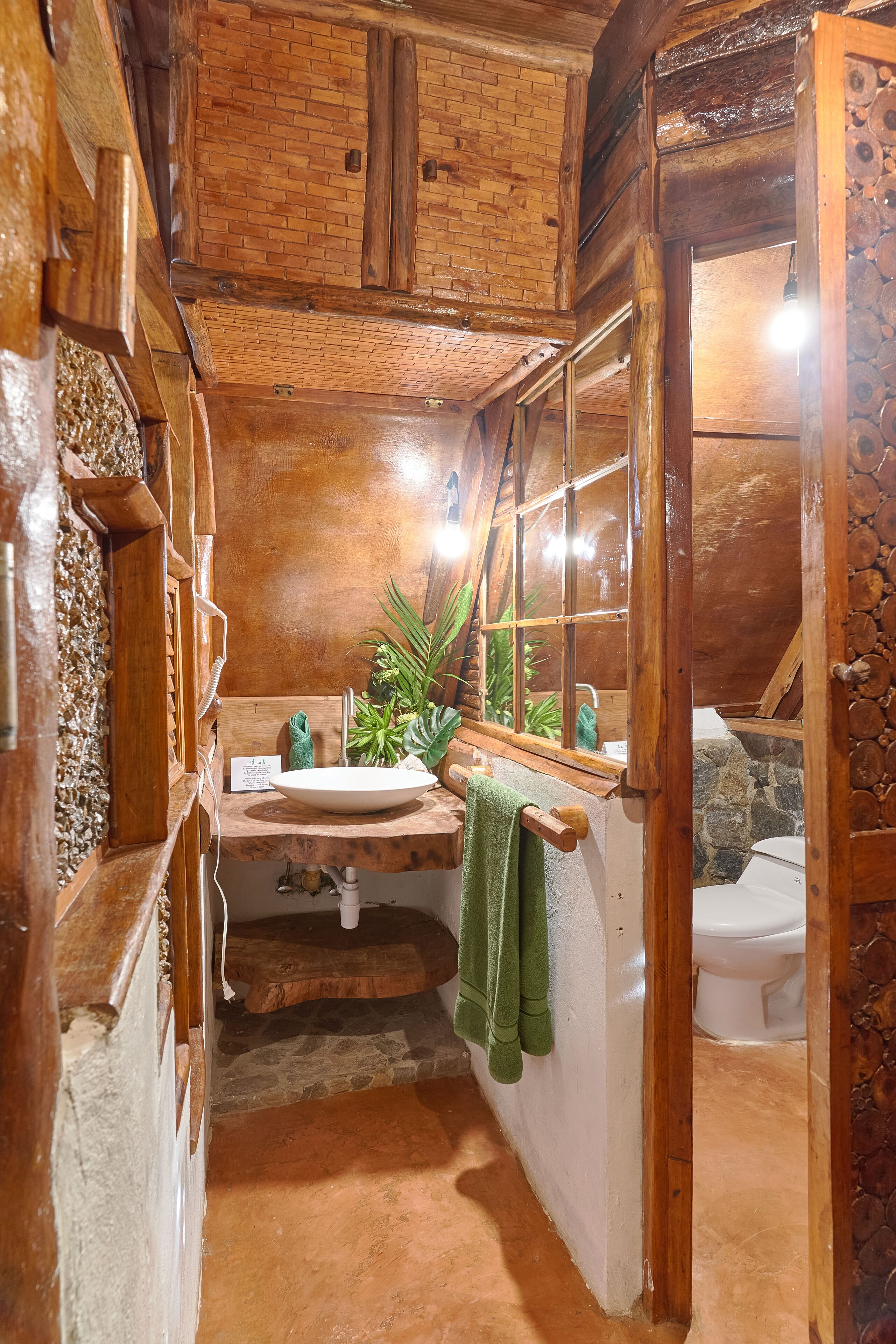 Een rustieke badkamer met houten inrichting, een stenen muur, een wastafel en een toilet.