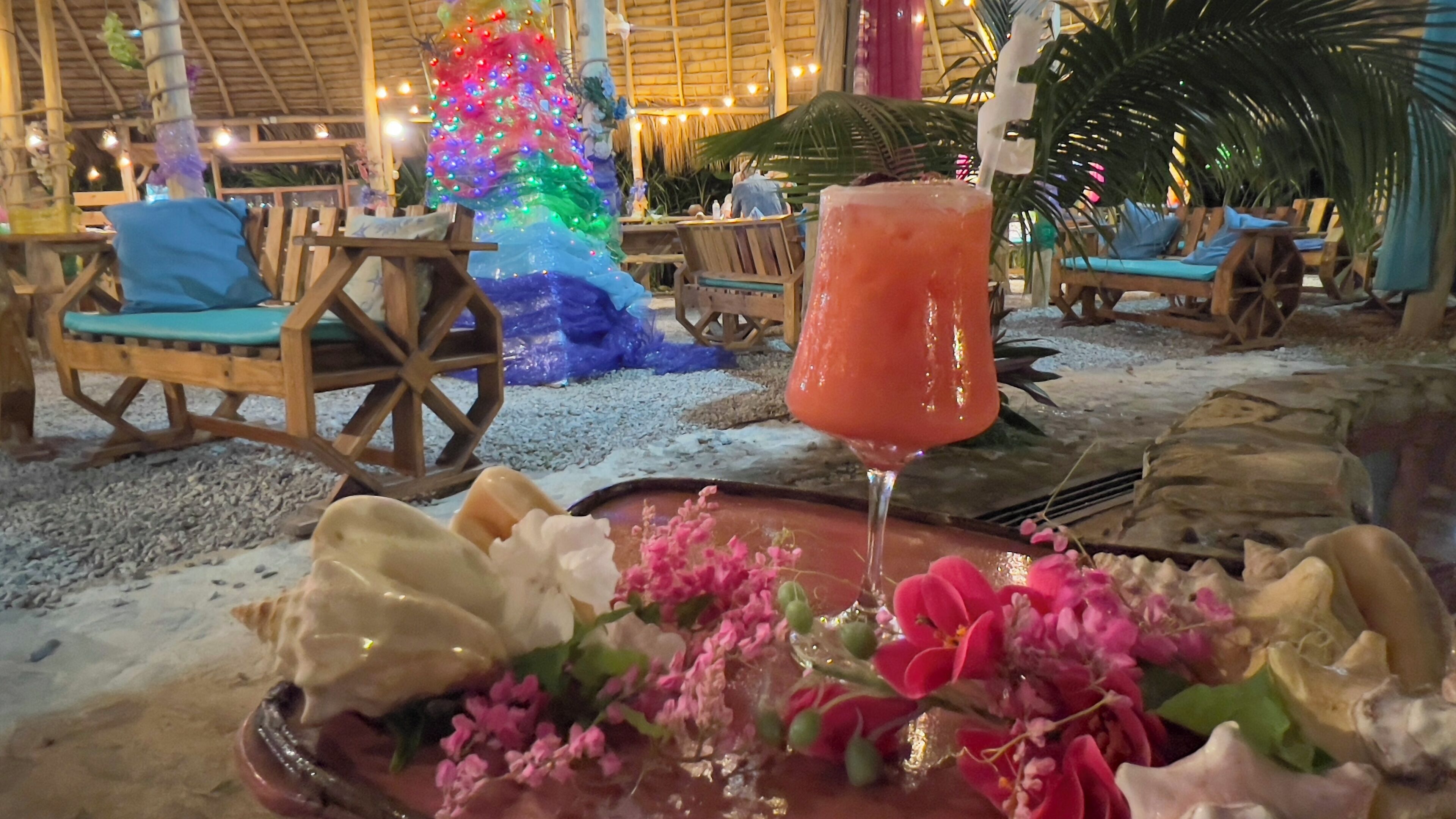 Uma área de estar ao ar livre com ambiente tropical, cadeiras de madeira e um centro de mesa decorativo.