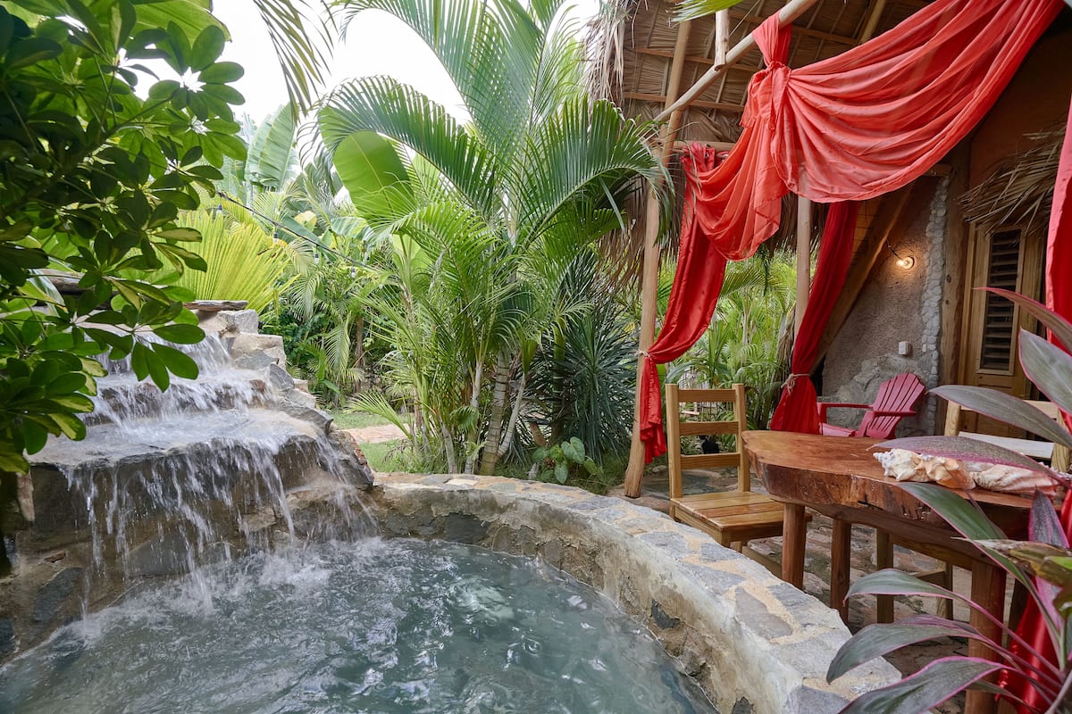 A hot spring area with a stone pool, wooden seating, and lush greenery.