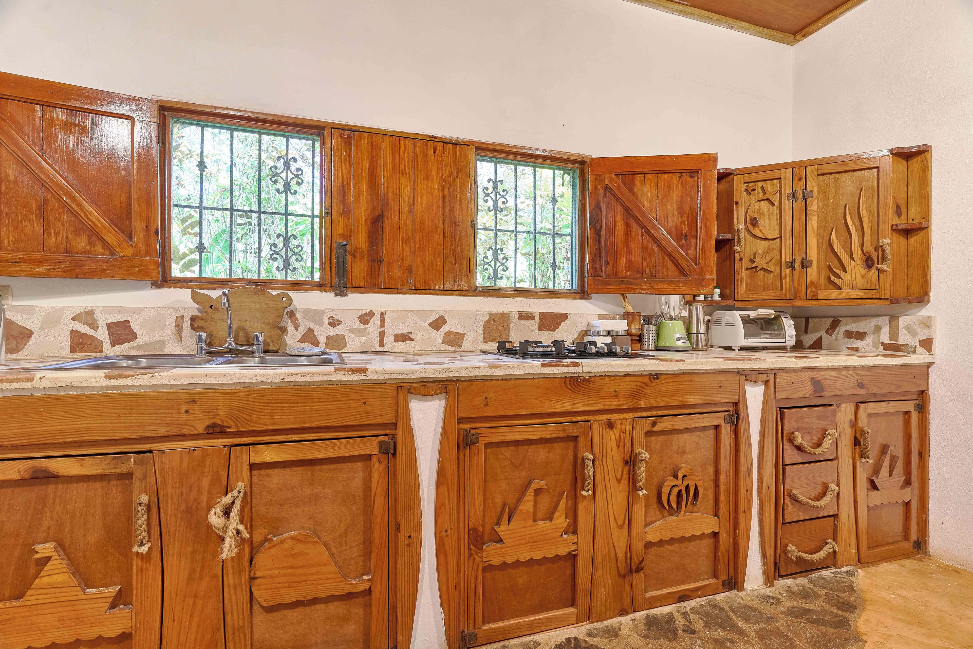 Cozinha com armários de madeira, painel de pedra e janela com grades.