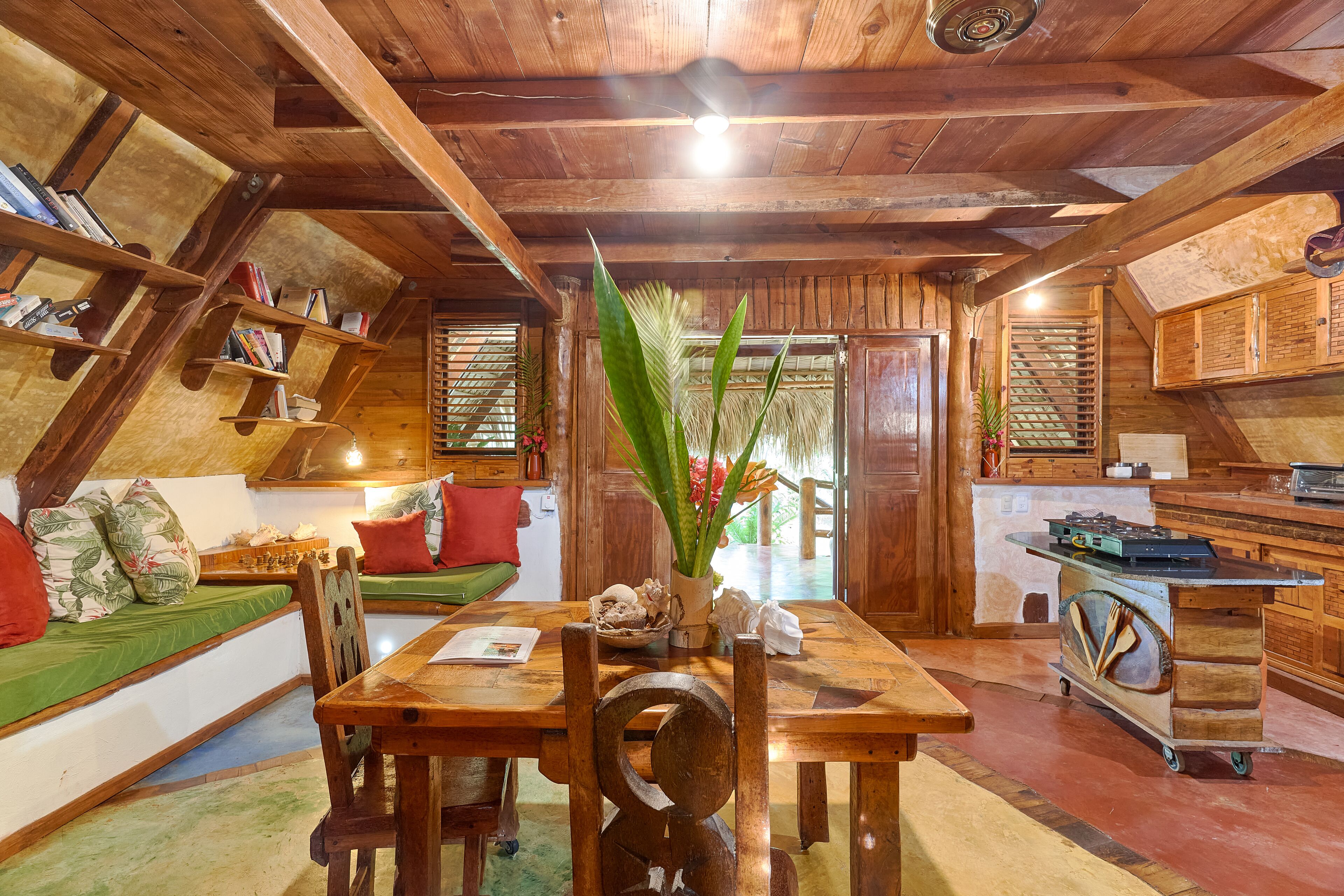 A cozy wooden interior with a dining table, chairs, a bookshelf, and a green sofa.