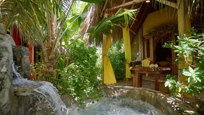 A tropical setting with a stone water feature, wooden furniture, and a thatched-roof structure. -  CHALET TROPICAL Hotel & Pool Bar Restaurant (Las Galeras)