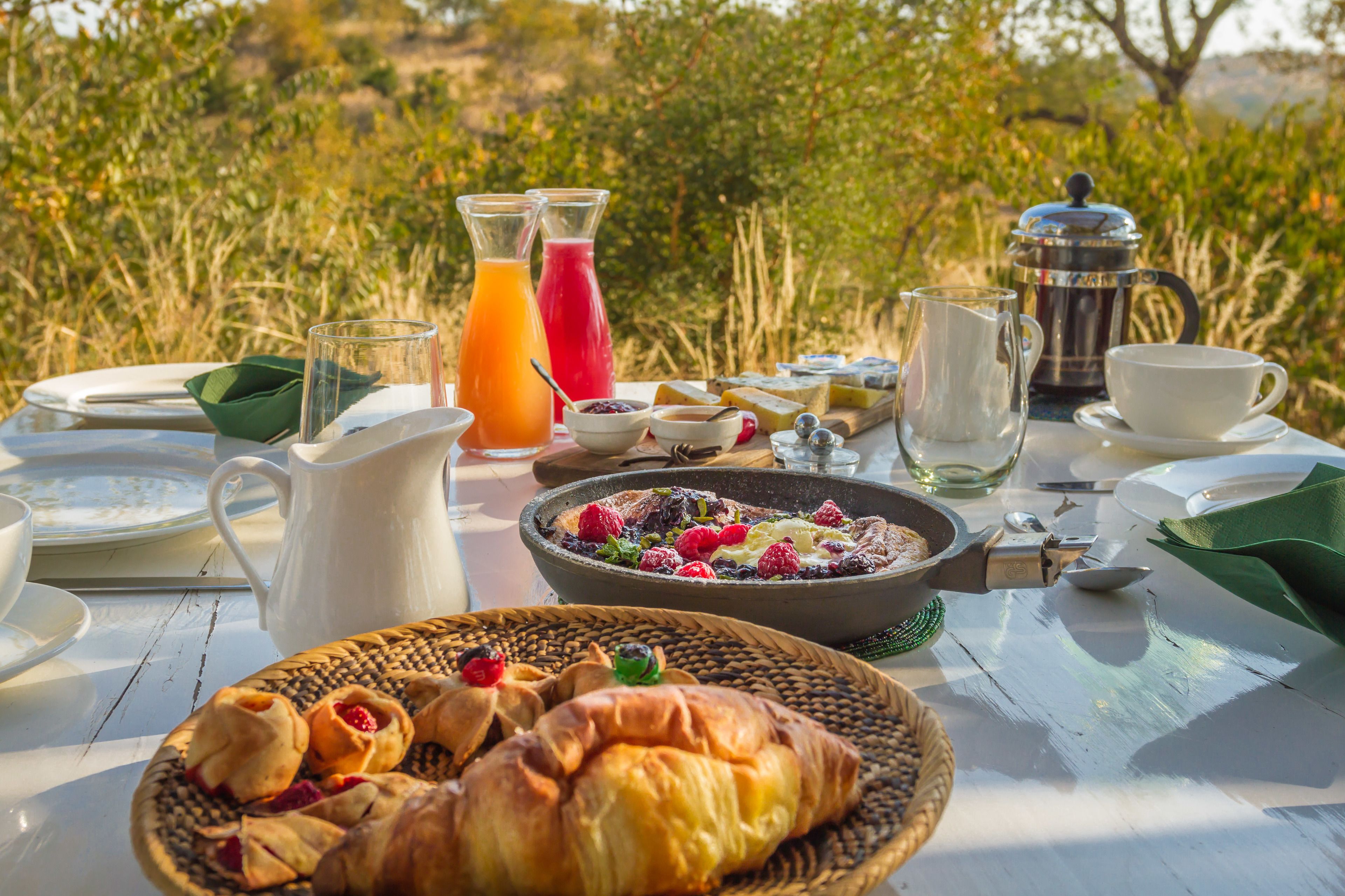 Ein Frühstückstisch im Freien mit Croissants, Obsttorte und einer Kaffeekanne.