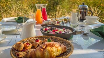 Ein Frühstückstisch im Freien mit Croissants, Obsttorte und einer Kaffeekanne.