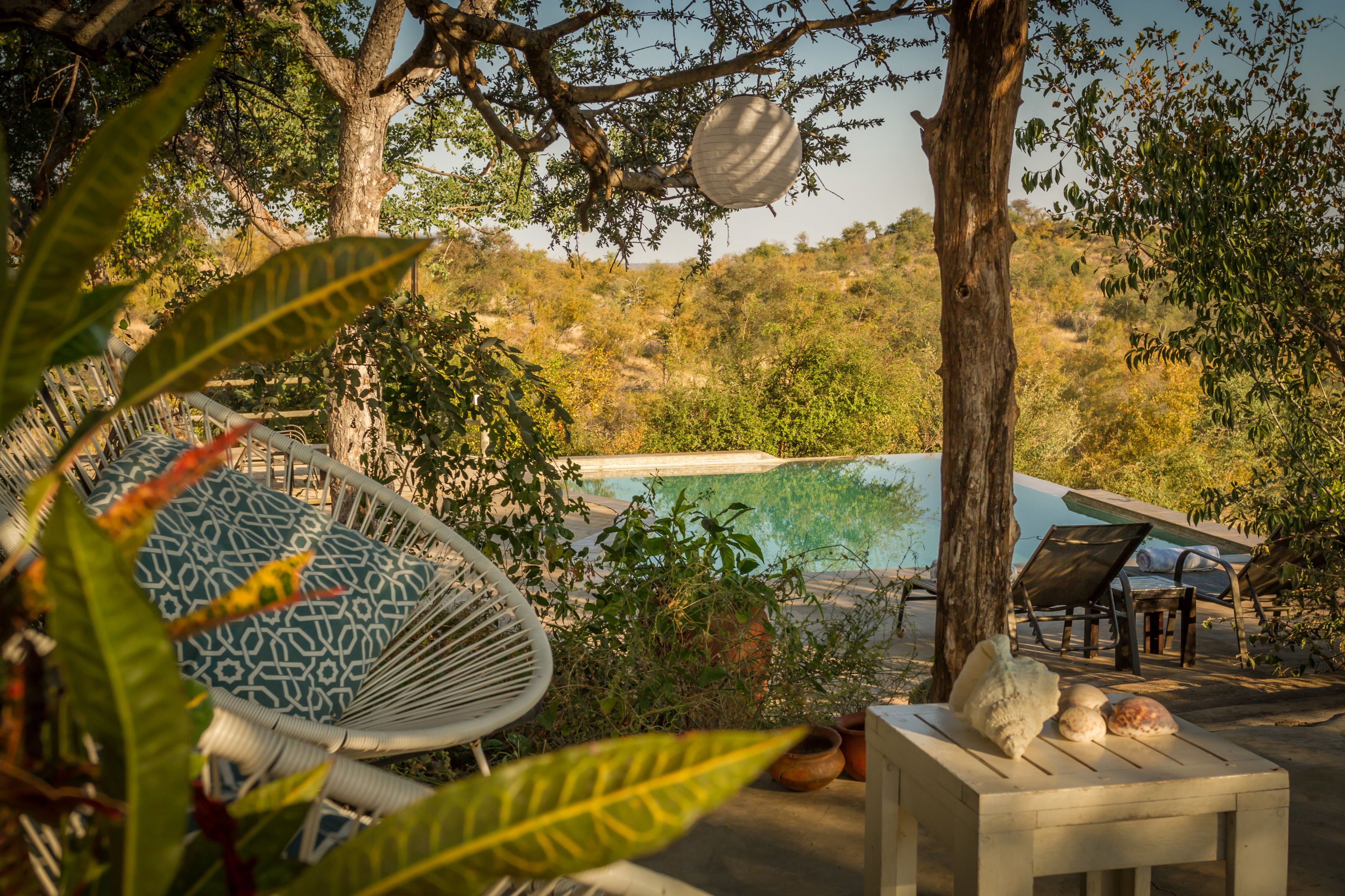 Zona junto a la piscina con una hamaca, sillas de descanso y vistas a un paisaje natural.