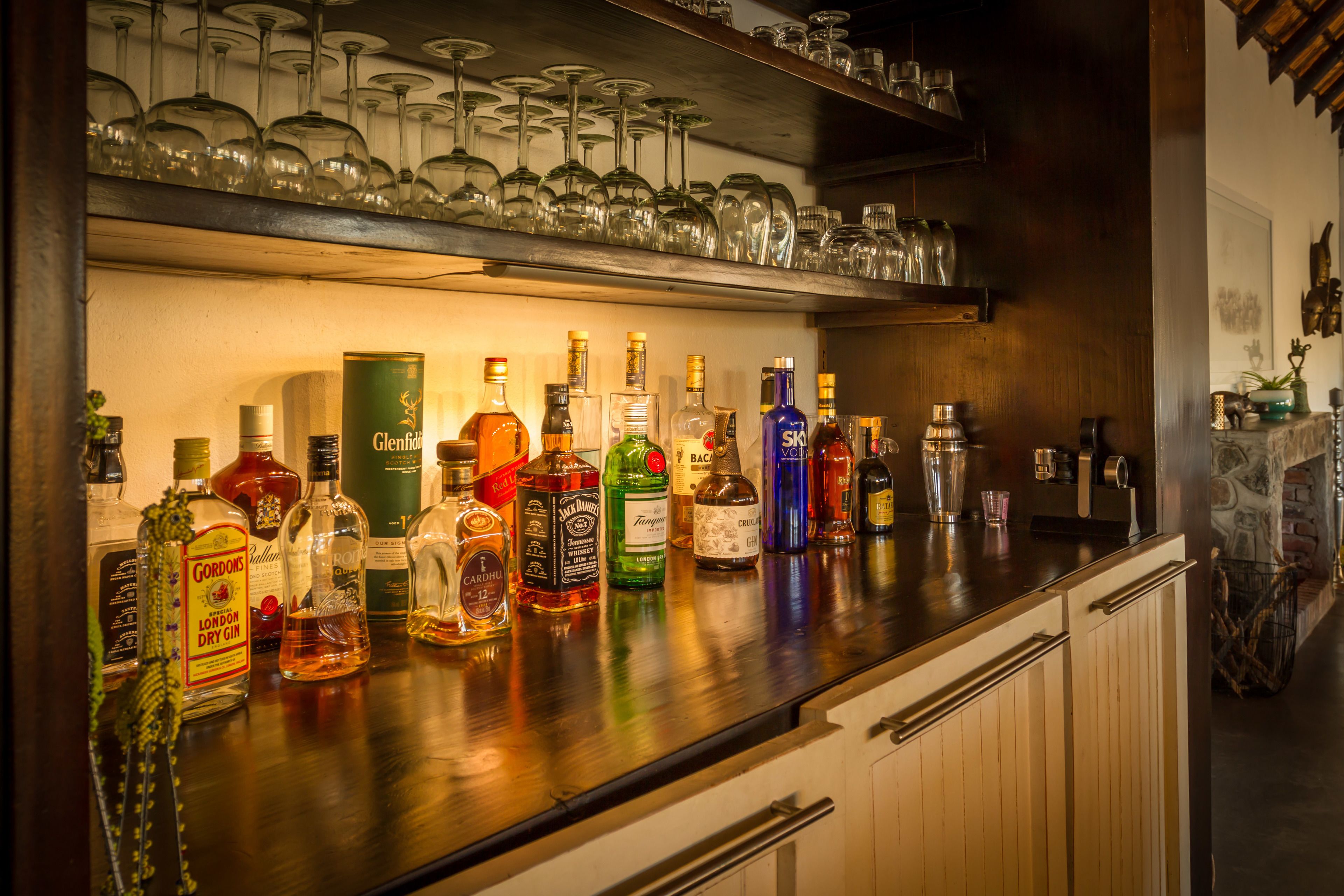 A bar area with various bottles of alcohol, glasses, and a shelf with wine glasses.