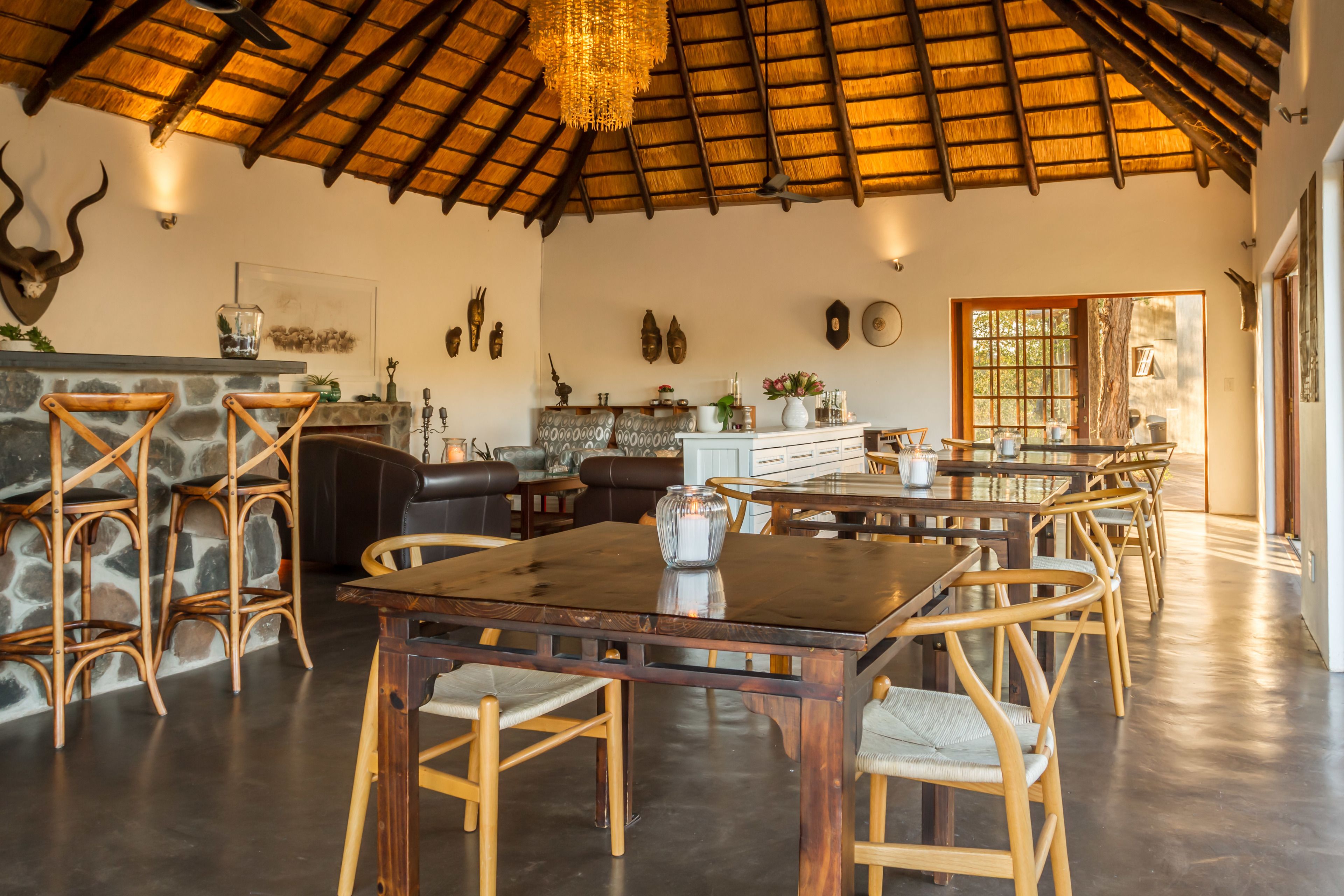 A spacious dining area with a high ceiling and a thatched roof, featuring a long wooden table and wicker chairs.