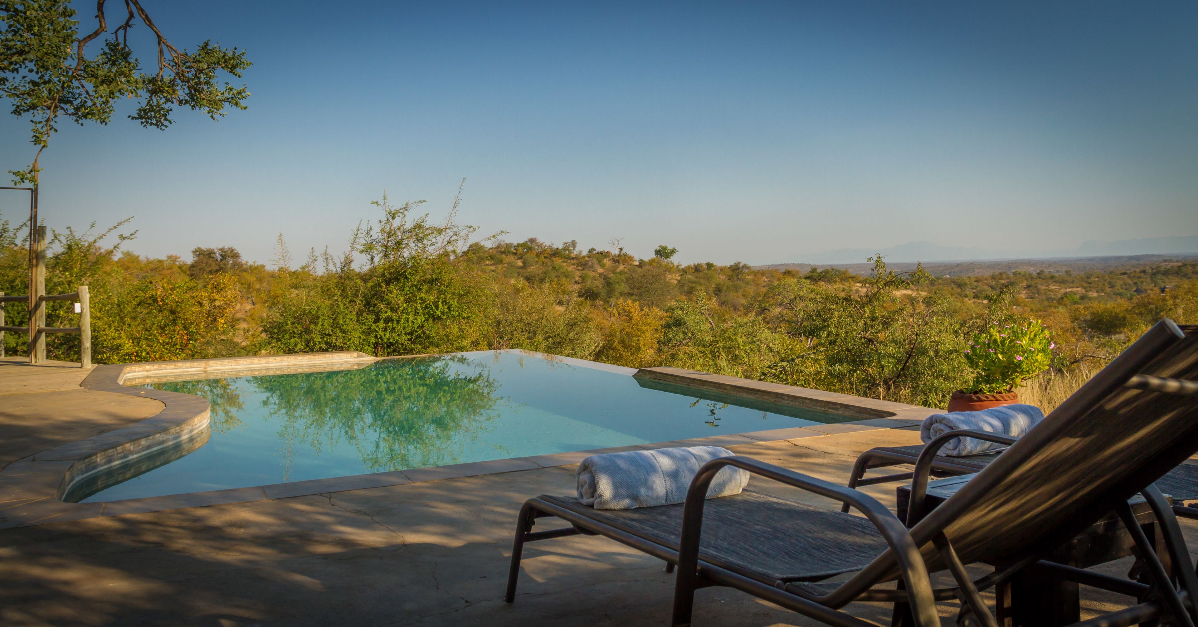 Une piscine entourée de chaises longues, de verdure et offrant une vue sur des collines lointaines.