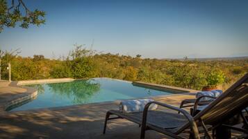 Une piscine entourée de chaises longues, de verdure et offrant une vue sur des collines lointaines.