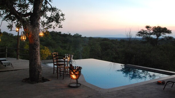 Ein Infinity-Pool mit Landschaftsblick, umgeben von einer Holzterrasse mit Sitzgelegenheiten und einer Feuerstelle.