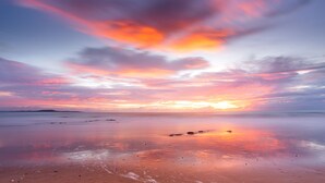 Une plage au coucher du soleil, avec une eau calme et une terre lointaine à l’horizon.
