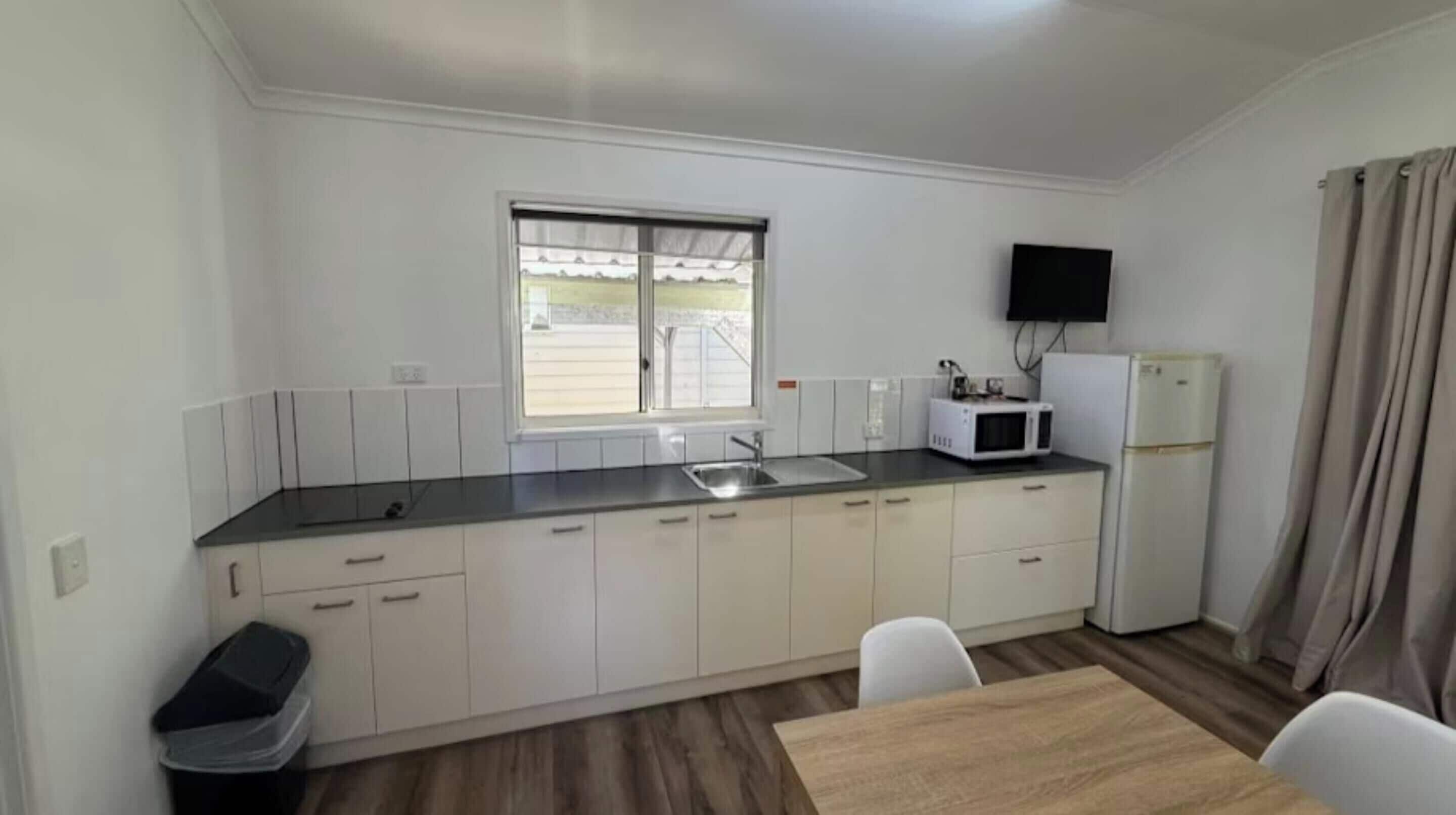 A compact kitchen with a window, a microwave, a refrigerator, and a dining area with a table and chairs.