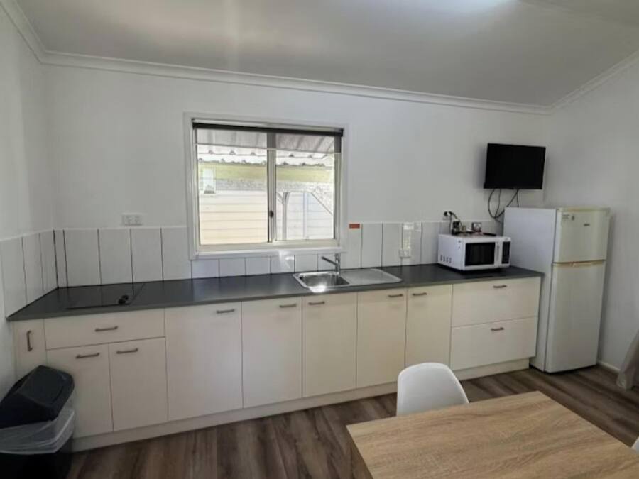 Cocina compacta con ventana, microondas, refrigerador y comedor con mesa y sillas.