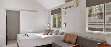 A modern bedroom with a bed, a sofa, a dining table, and a ceiling fan.