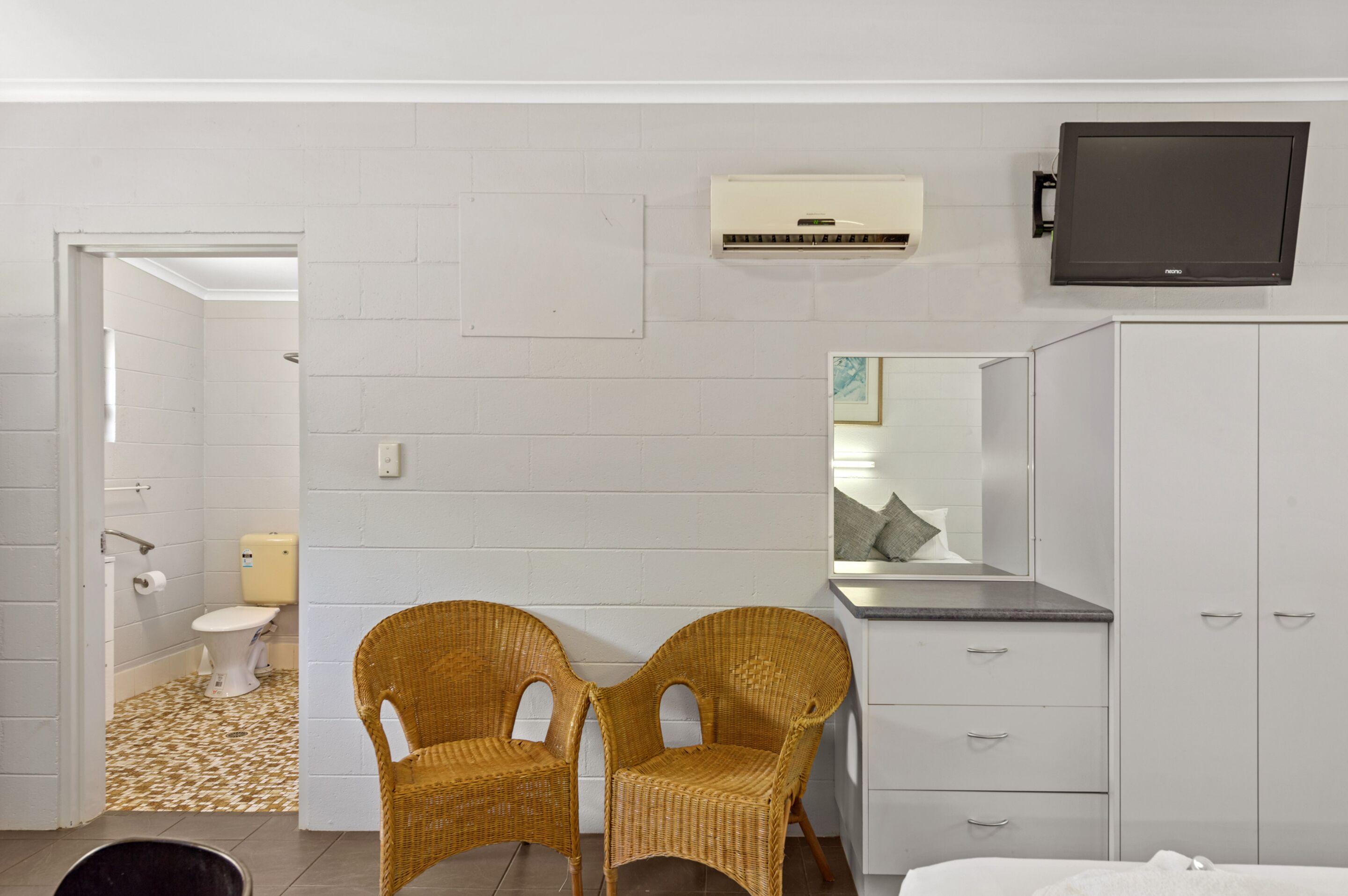 A bedroom with a bed, a dresser, a television, and a bathroom visible through an open door.