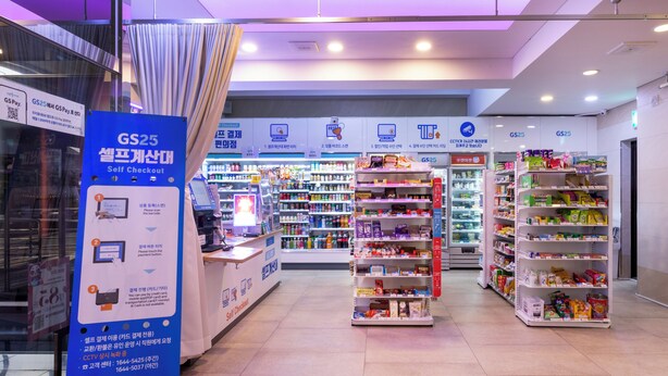 A self-checkout area with a blue sign, shelves stocked with various products, and a checkout counter. - Sea View (Jeju City)