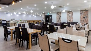 A spacious restaurant with multiple dining tables and chairs, a kitchen area, and a brick accent wall. - Sea View (Jeju City)