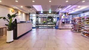 A self-service checkout area with a variety of products on shelves, a reception desk with a clock, and a glass door entrance. - Sea View (Jeju City)