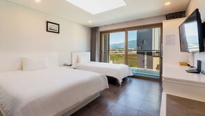 A hotel room with two beds, a television, a desk, and a large window with a view of the countryside. - Sea View (Jeju City)