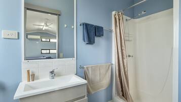 Un baño con un lavamanos blanco, un espejo, un perchero con dos toallas y una ducha con cortina color crema.