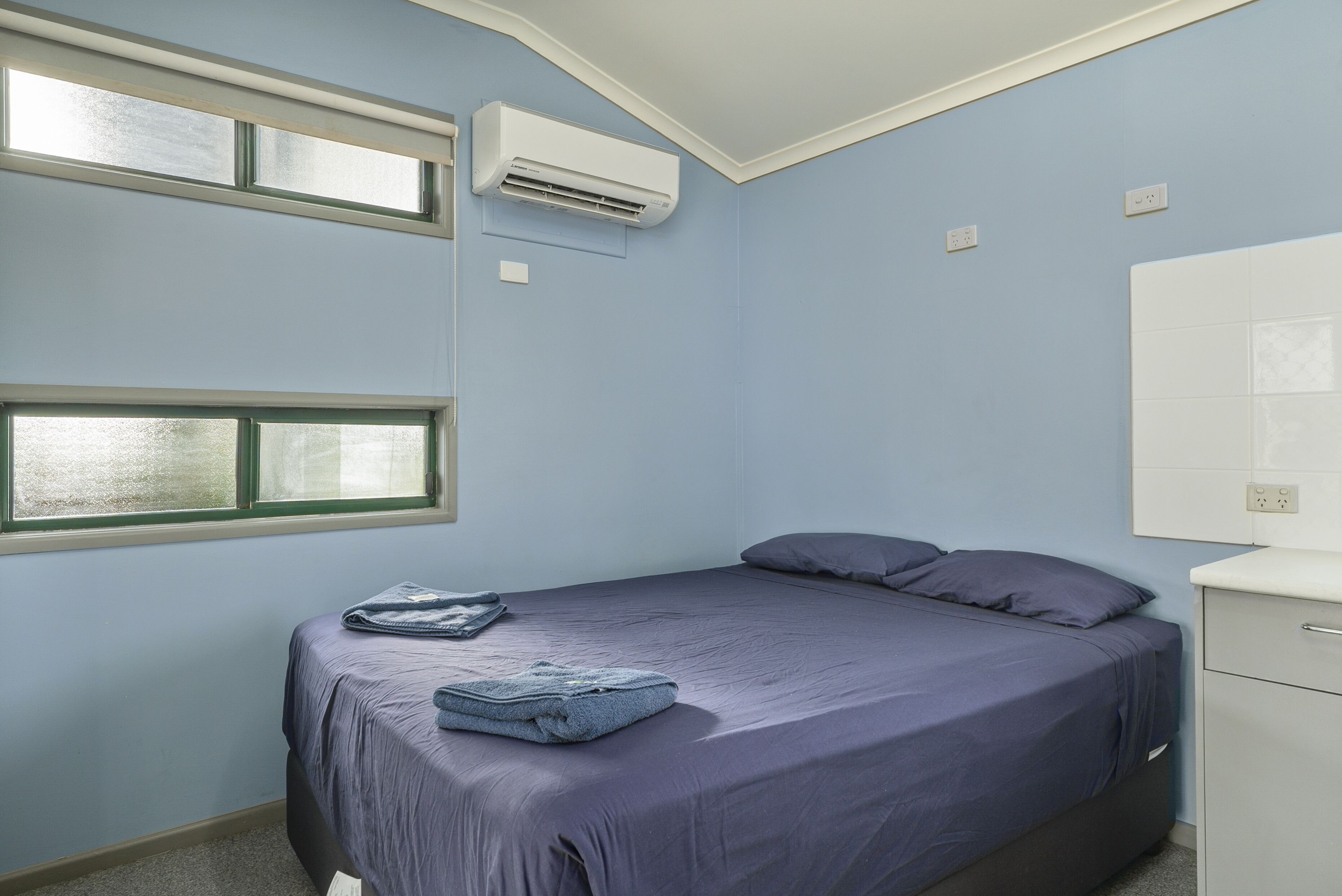 A bedroom with a bed, a window, an air conditioner, and a white cabinet.