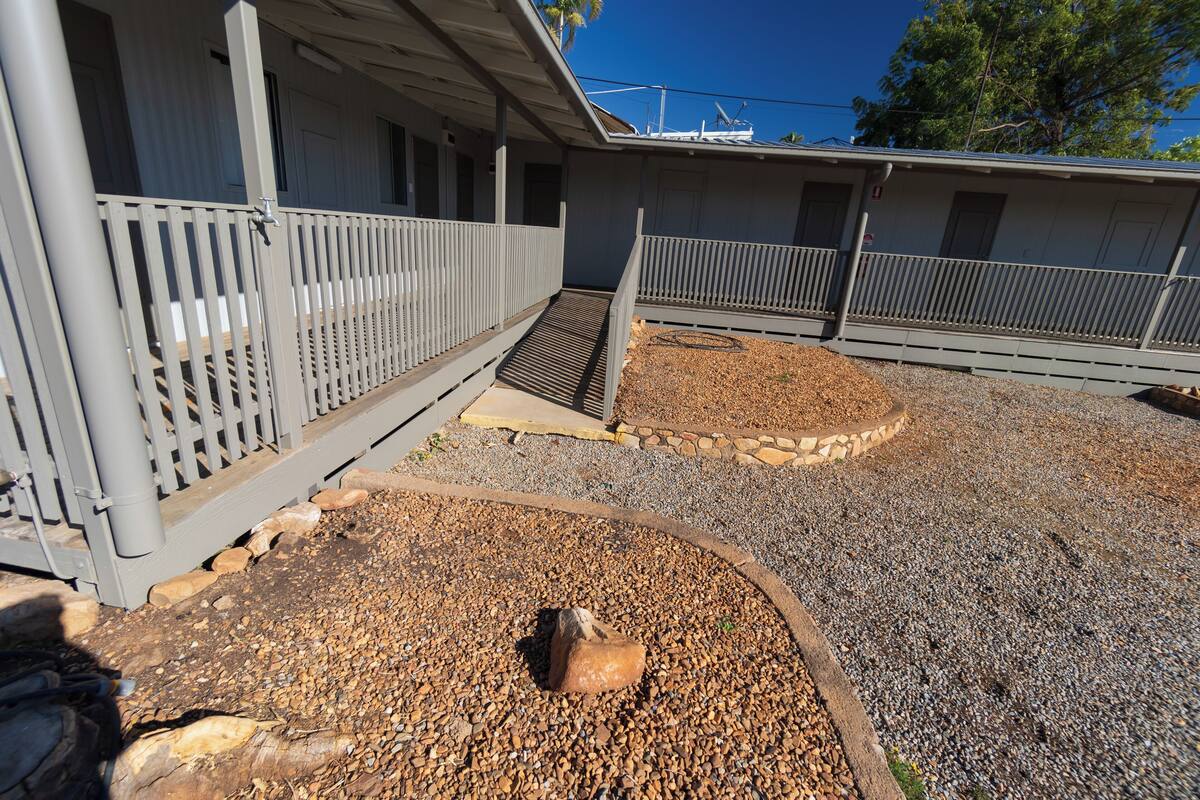 A building with a covered porch, a gravel driveway, and a small garden area with a rock centerpiece.