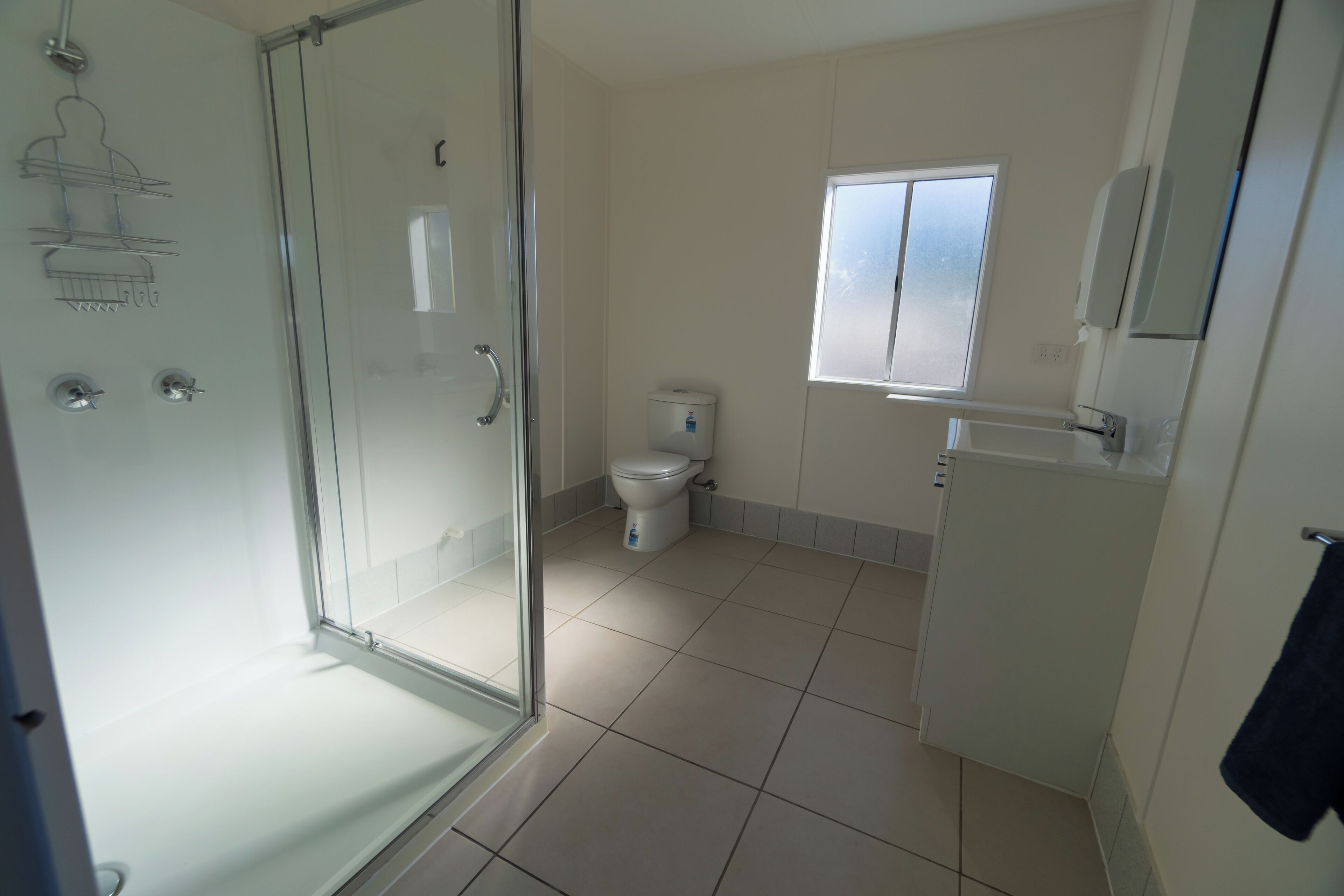 A bathroom with a glass shower enclosure, a toilet, and a window.