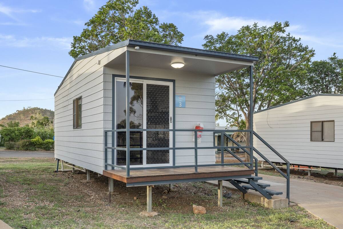 A small, single-story cabin with a covered porch, a window, and a door with a mesh screen.