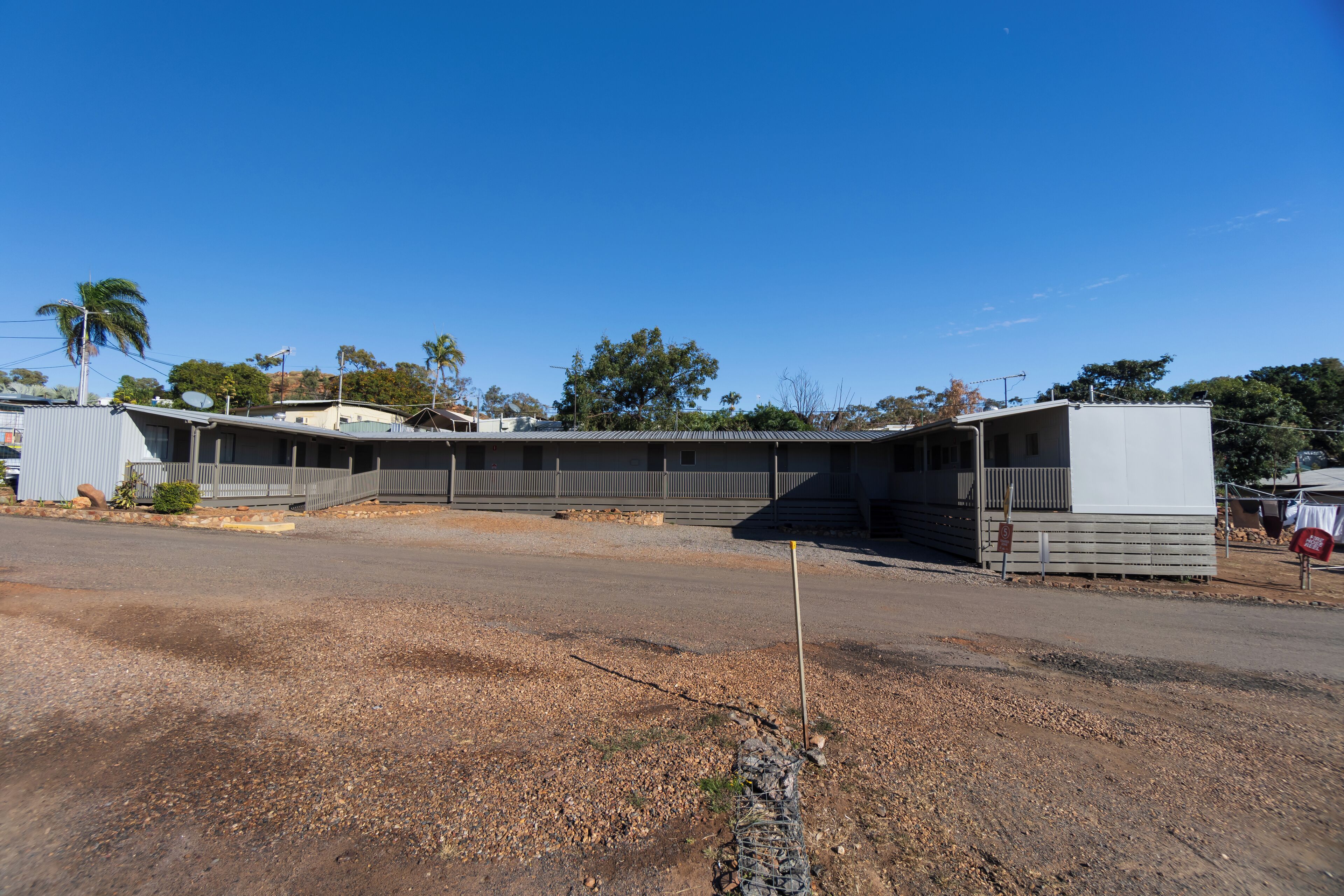 A building with a flat roof, a covered outdoor area, and a gravel driveway.