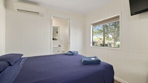 Un dormitorio con cama, ventana, televisor y puerta que da a un baño.