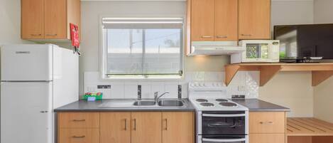 A modern kitchen with wooden cabinets, a built-in microwave, a refrigerator, and a window with blinds.