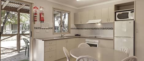 A modern kitchen with white cabinets, a built-in microwave, and a refrigerator. There is a dining table with four chairs and a window providing natural light.
