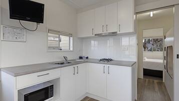 Cocina compacta con armarios blancos, microondas integrado, estufa a gas y televisor de pantalla plana sobre el lavabo.