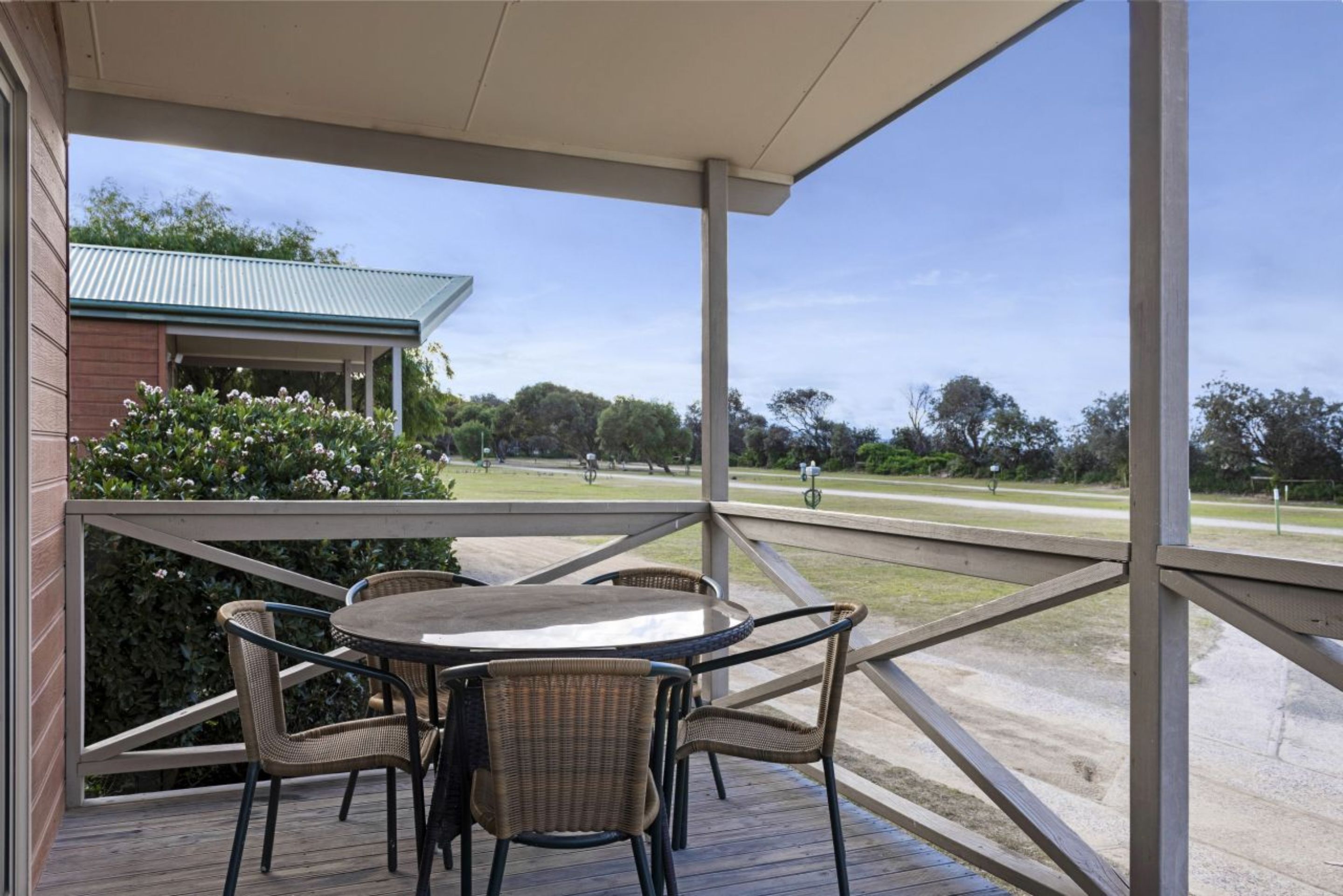 A covered outdoor area with a table and chairs, a view of a park, and a building with a green roof.